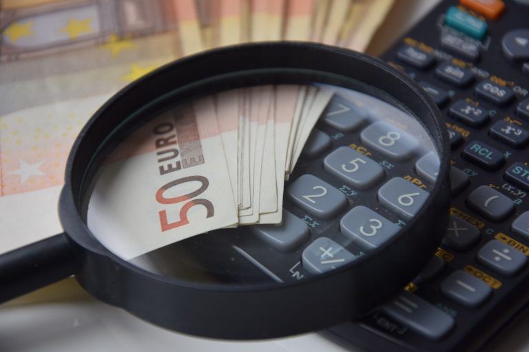 50-Euro-Scheine liegen unter einer schwarzen Lupe sowie auf einem Taschenrechner als Symbol für das Finden des richtigen Mietpreises.