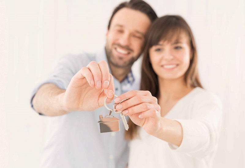 Ein junges braunhaariges Paar hält einen Schlüssel und lächelt