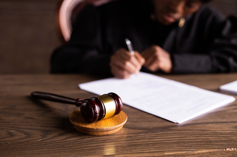 Eine Richterin füllt auf einem braunen Holztisch ein Formular aus. Davor liegt ein Gerichtshammer
