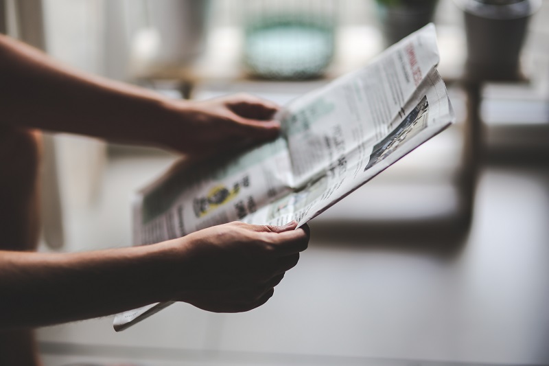 Zwei Hände halten eine Zeitung, in der auf eine Immobilie aufmerksam gemacht wird
